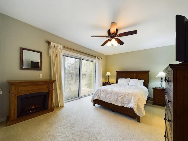 bedroom featuring light colored carpet, a ceiling fan, a lit fireplace, and access to exterior
