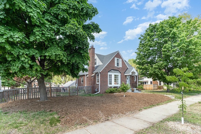 tudor-style house with brick siding, fence, and a chimney