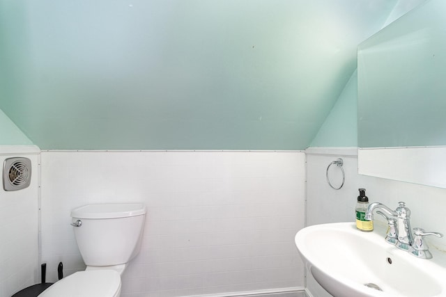 half bath with a sink, toilet, tile walls, a wainscoted wall, and lofted ceiling