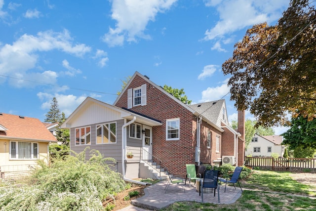 view of front of house with a patio area, fence, brick siding, and a cooling unit