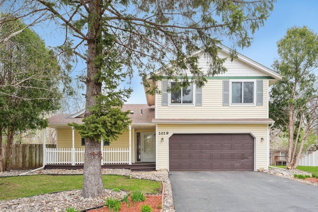traditional-style house with an attached garage, aphalt driveway, fence, and covered porch