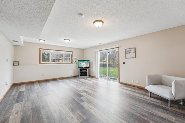 living area with baseboards, a textured ceiling, and wood finished floors