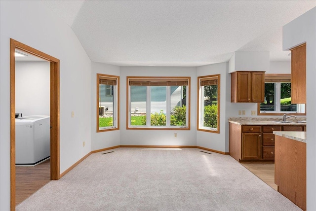 2228 White Pine Ct, Hudson, WI 54016 - kitchen featuring washer / dryer, brown cabinetry, plenty of natural light, light colored carpet, and a textured ceiling