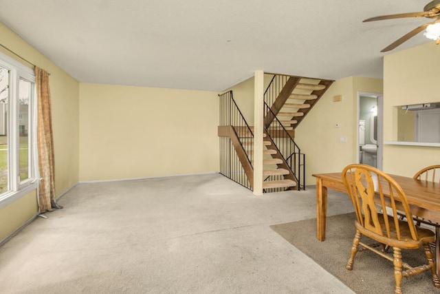 carpeted dining area with baseboards, stairway, and ceiling fan