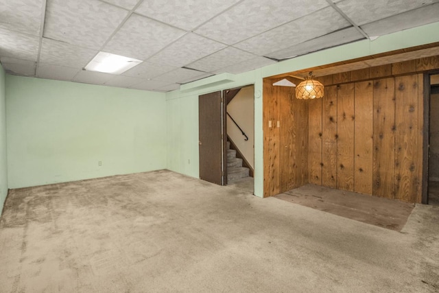 finished basement featuring wood walls, a drop ceiling, carpet flooring, and stairs