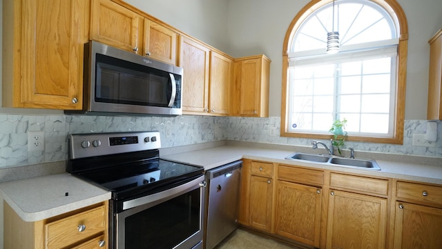 kitchen with stainless steel appliances, decorative backsplash, light countertops, and a sink