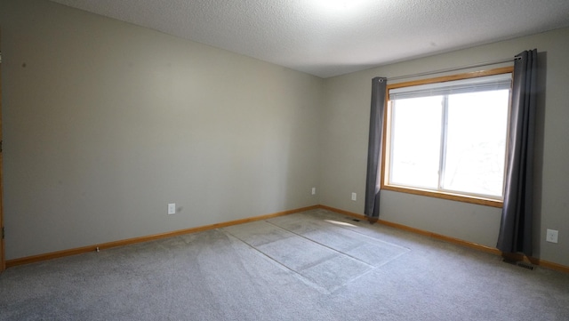 spare room featuring light colored carpet, visible vents, baseboards, and a textured ceiling