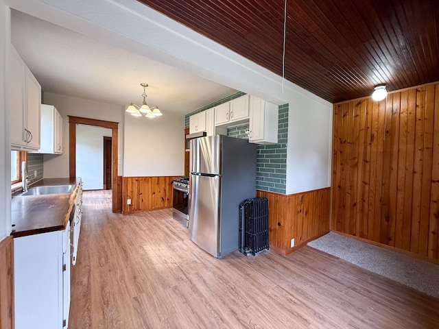 329 2nd St, Le Sueur, MN 56058 - kitchen with white cabinets, stainless steel appliances, light wood-type flooring, a chandelier, and wooden walls