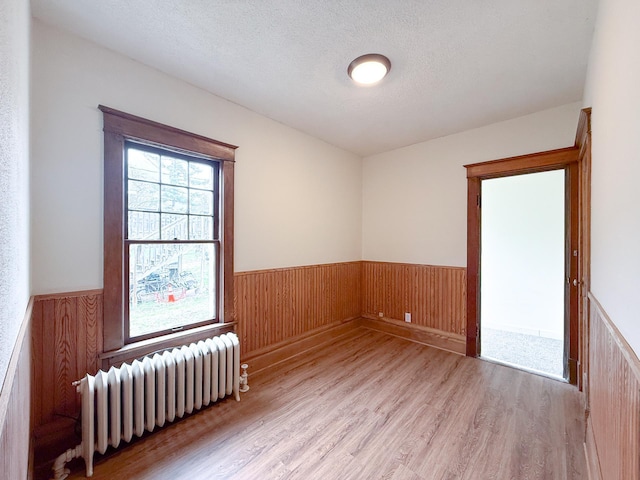 329 2nd St, Le Sueur, MN 56058 - empty room with radiator heating unit, a textured ceiling, wood finished floors, and wainscoting