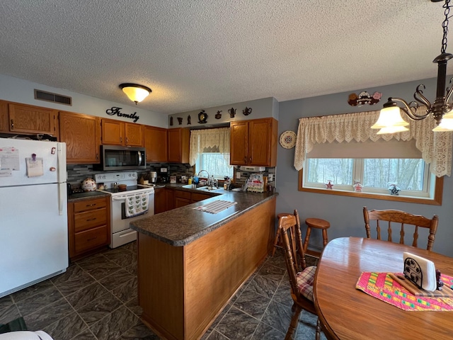 kitchen featuring brown cabinets, visible vents, white appliances, and a peninsula