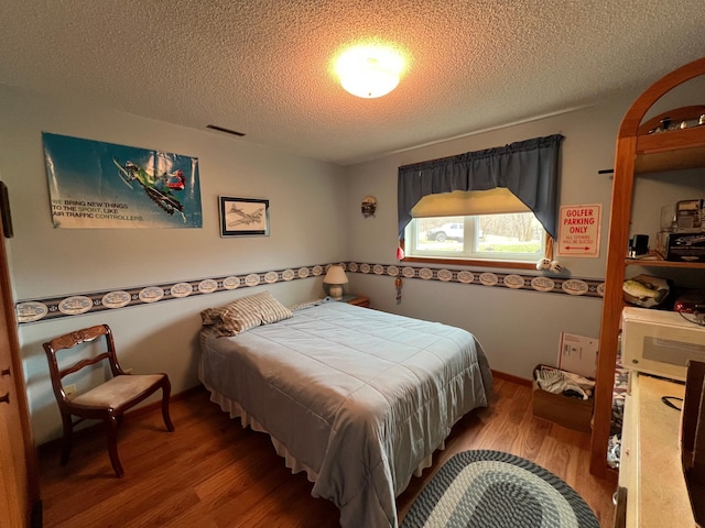 bedroom featuring a textured ceiling, visible vents, and wood finished floors