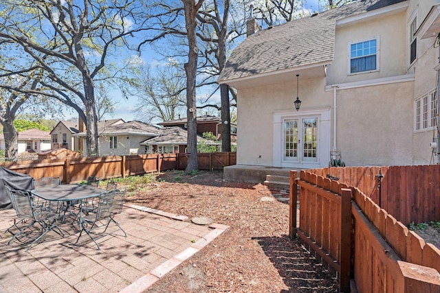 rear view of property featuring french doors, a shingled roof, stucco siding, a fenced backyard, and a patio