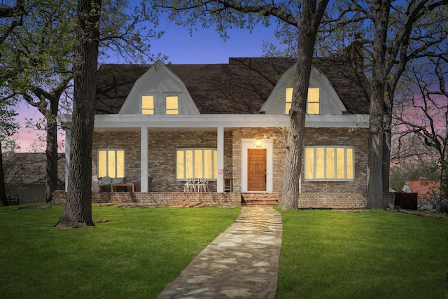 view of front of home with brick siding, a yard, and covered porch
