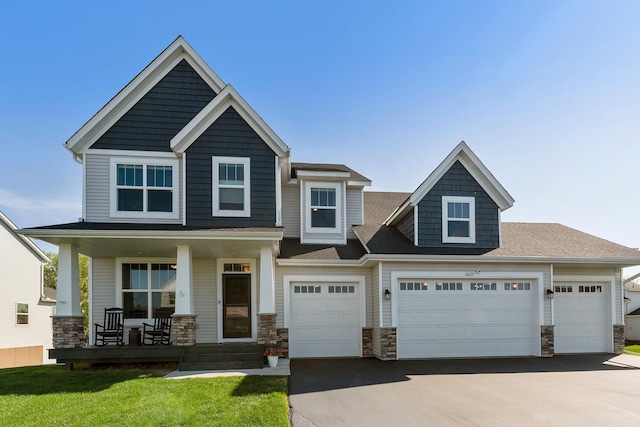 craftsman-style house with covered porch, stone siding, driveway, an attached garage, and a front yard