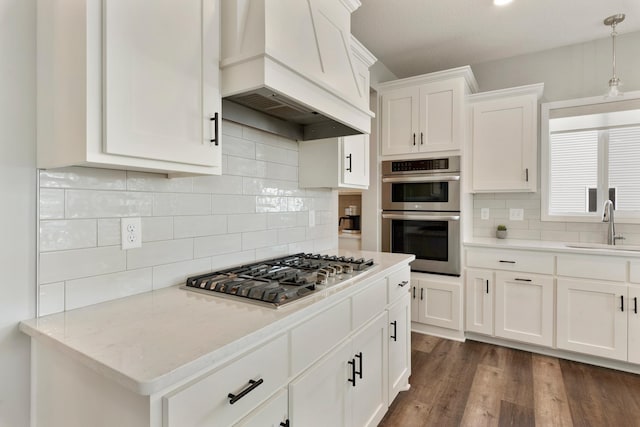kitchen featuring appliances with stainless steel finishes, premium range hood, a sink, white cabinetry, and decorative backsplash