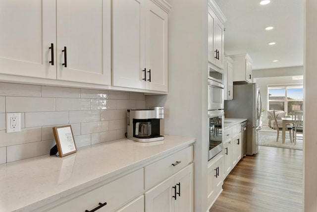 kitchen with white cabinetry, decorative backsplash, recessed lighting, light wood-style flooring, and light stone countertops