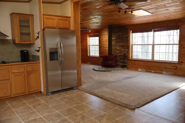 kitchen featuring stainless steel refrigerator with ice dispenser, wood ceiling, a wood stove, ceiling fan, and wood walls
