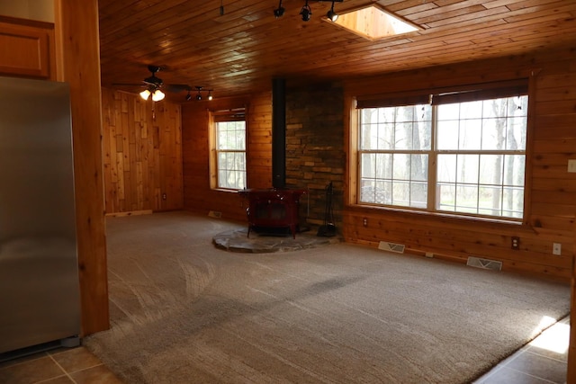 unfurnished living room featuring wooden walls, a wood stove, wooden ceiling, rail lighting, and a skylight