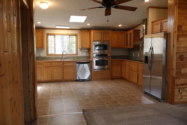 kitchen featuring appliances with stainless steel finishes, wall chimney range hood, a ceiling fan, a sink, and tile patterned flooring
