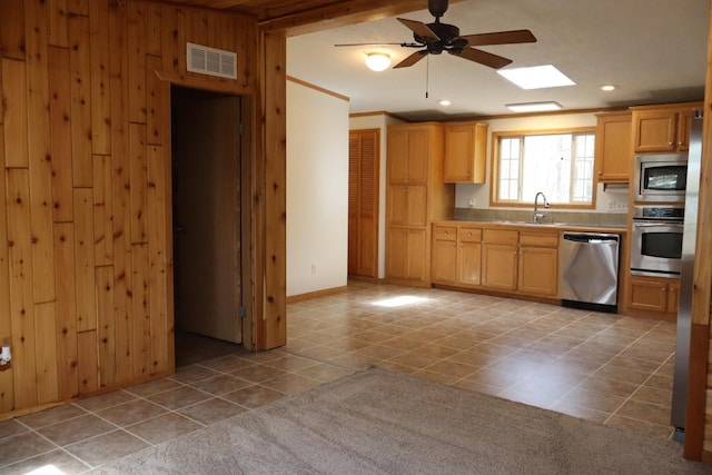 kitchen featuring appliances with stainless steel finishes, light tile patterned floors, a sink, a ceiling fan, and wooden walls