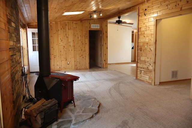 unfurnished room with a wood stove, wooden walls, wooden ceiling, ceiling fan, and baseboards