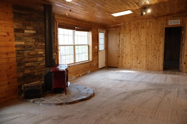 empty room with a wood stove, carpet floors, wooden walls, and wood ceiling