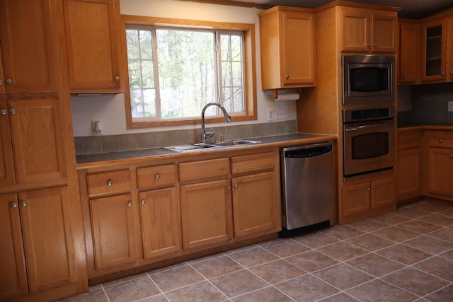 kitchen with appliances with stainless steel finishes, a sink, tile counters, light tile patterned floors, and tasteful backsplash