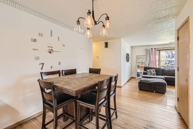 dining area with light wood-style floors, a textured ceiling, baseboards, and a chandelier