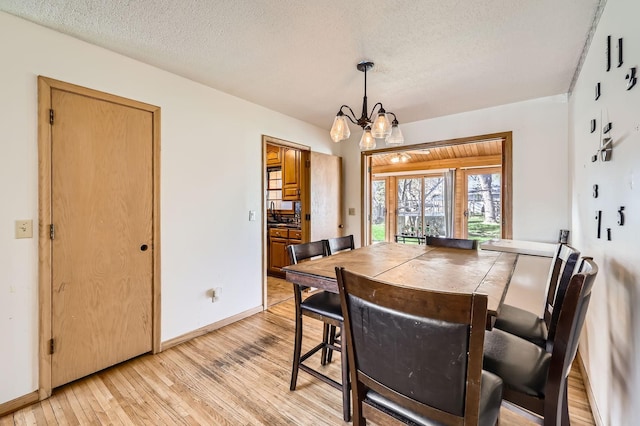dining space featuring an inviting chandelier, a textured ceiling, light wood finished floors, and baseboards