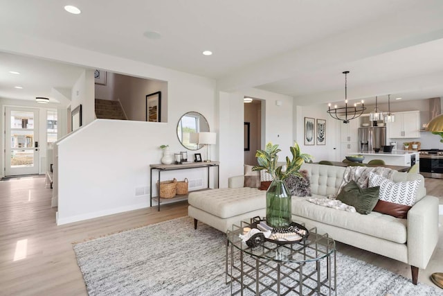 living room featuring light wood-type flooring, recessed lighting, a notable chandelier, and stairs