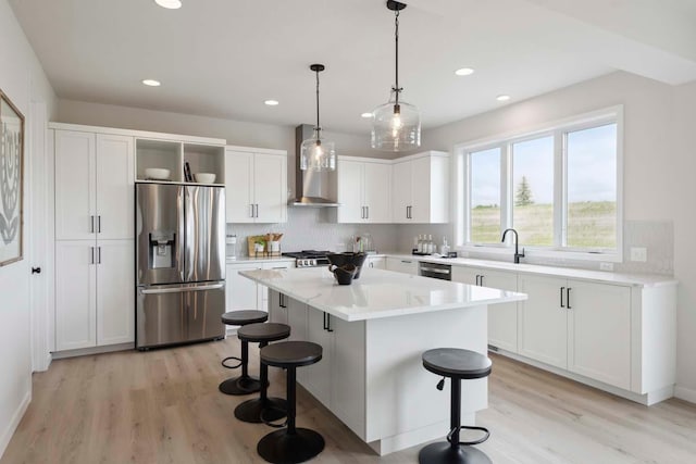 kitchen featuring stainless steel appliances, open shelves, light wood-type flooring, wall chimney exhaust hood, and a breakfast bar area