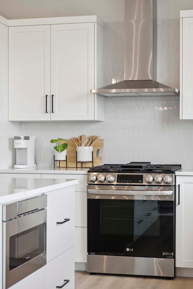 kitchen with wall chimney range hood, white cabinetry, tasteful backsplash, light countertops, and stainless steel gas range
