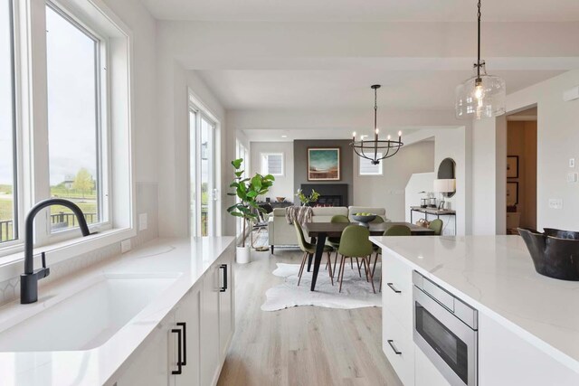 kitchen featuring stainless steel microwave, white cabinets, light wood-style flooring, a sink, and decorative light fixtures