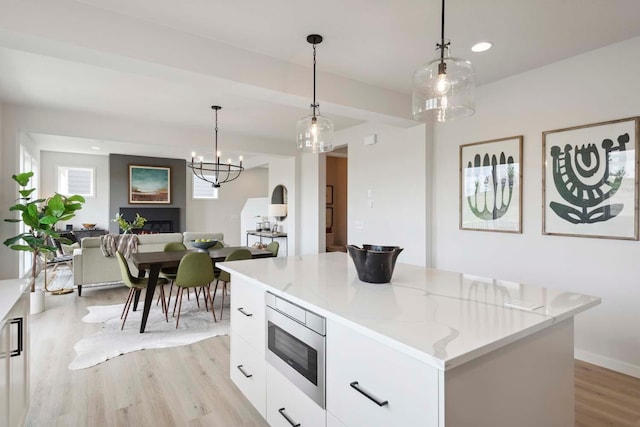 kitchen featuring stainless steel microwave, white cabinetry, light wood-style flooring, a center island, and modern cabinets