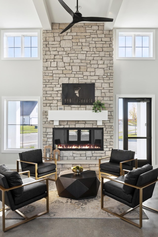 living area with a towering ceiling, a ceiling fan, a stone fireplace, and a healthy amount of sunlight