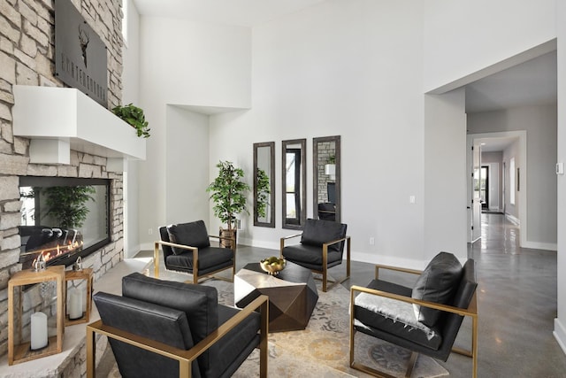 living room featuring a towering ceiling, concrete floors, a stone fireplace, and baseboards