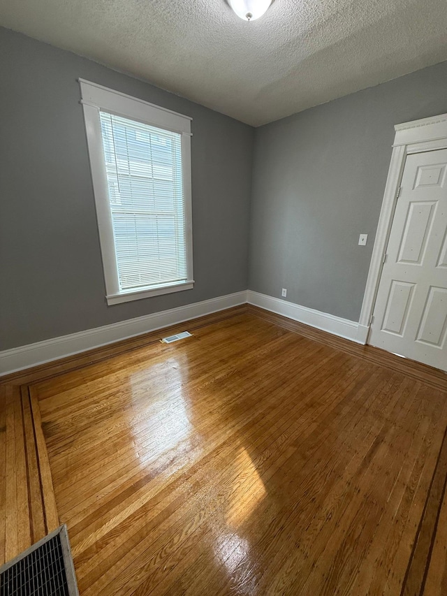 spare room featuring wood finished floors, baseboards, and a textured ceiling