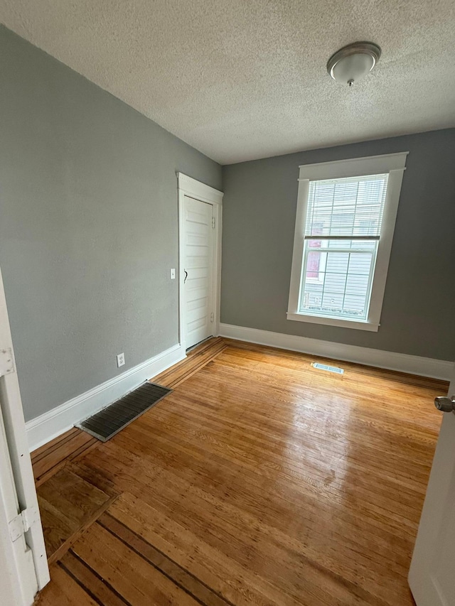 empty room featuring wood finished floors, baseboards, and a textured ceiling
