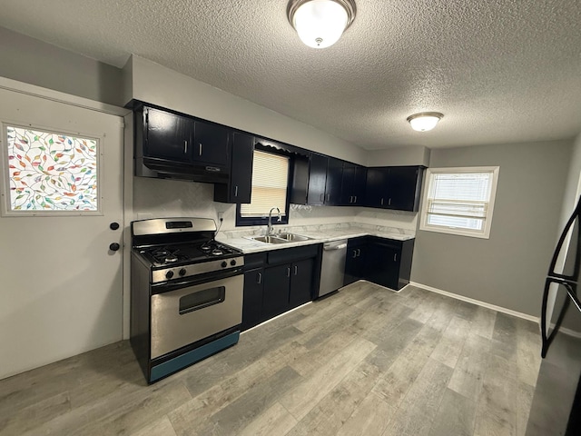 kitchen with appliances with stainless steel finishes, dark cabinets, a sink, light countertops, and a textured ceiling