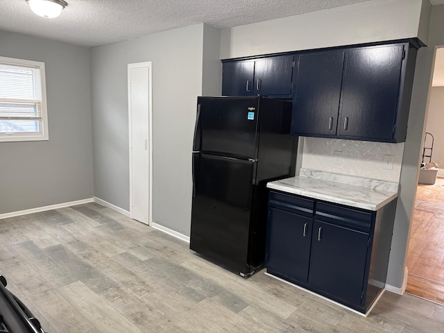 kitchen featuring freestanding refrigerator, light wood-style flooring, light countertops, a textured ceiling, and baseboards