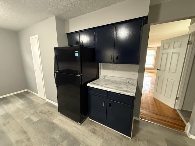 kitchen featuring dark cabinetry, freestanding refrigerator, light countertops, light wood finished floors, and a textured ceiling