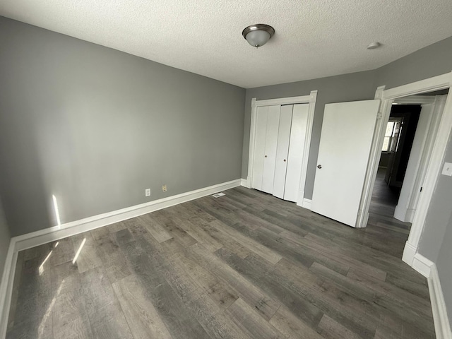 unfurnished bedroom featuring dark wood-style floors, a textured ceiling, baseboards, and a closet