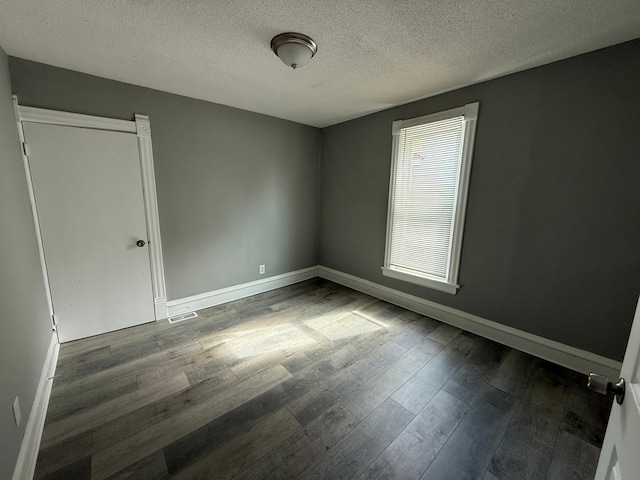 unfurnished room featuring a textured ceiling, wood finished floors, and baseboards
