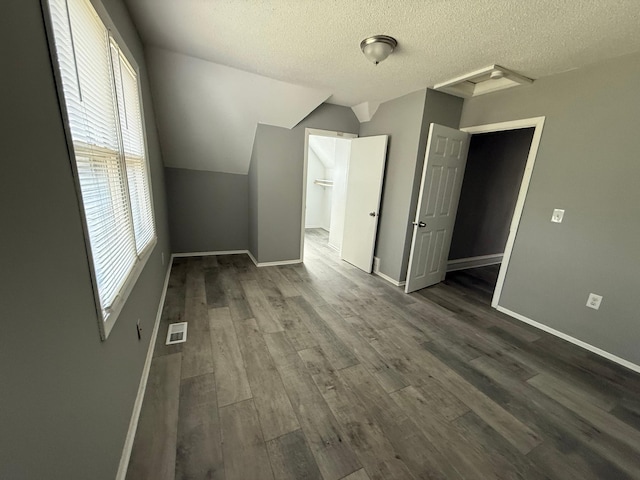 bonus room featuring dark wood finished floors, baseboards, a textured ceiling, and lofted ceiling