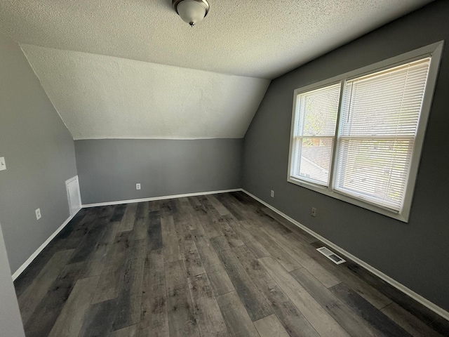 additional living space featuring a textured ceiling, vaulted ceiling, dark wood finished floors, and baseboards