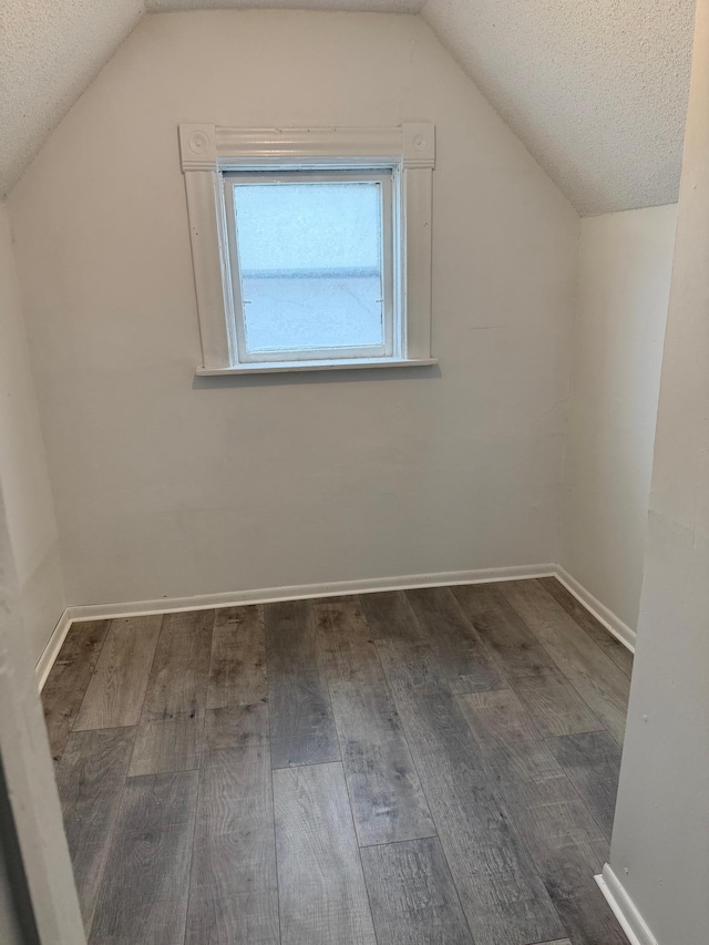 additional living space featuring vaulted ceiling, wood finished floors, baseboards, and a textured ceiling