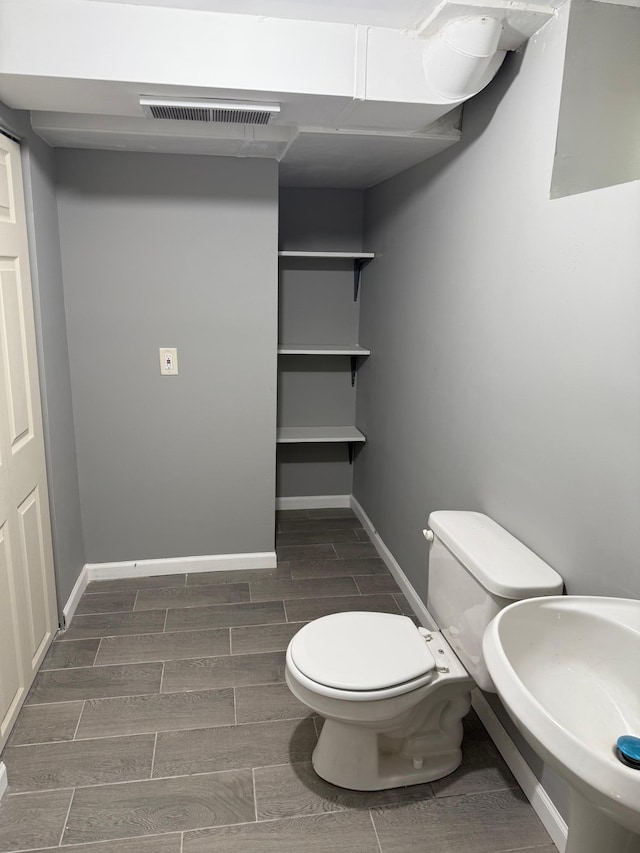 half bathroom with wood finish floors, toilet, baseboards, and a sink