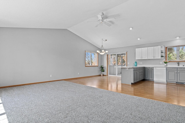 unfurnished living room with light carpet, a chandelier, a ceiling fan, a sink, and lofted ceiling