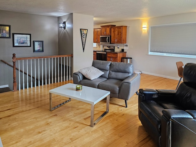 living room with a textured ceiling, baseboards, and light wood finished floors