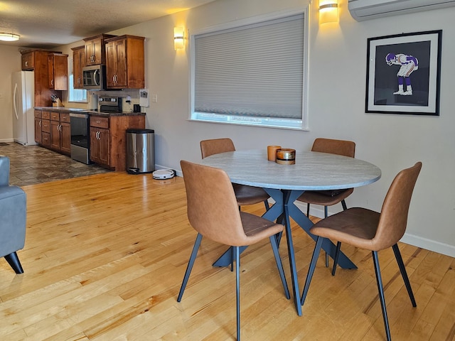 dining space with baseboards, a wall unit AC, and light wood finished floors